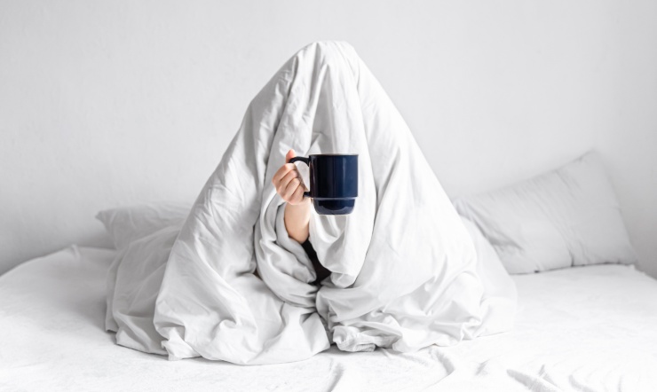 Una persona nel letto con il caffè in mano che non riesce a svegliarsi