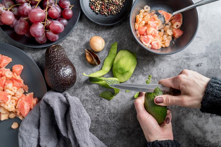Una persona taglia un avocado e prepara una Poke Bowl 