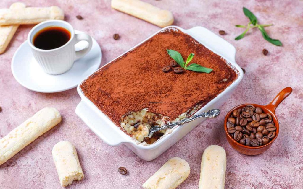 Una teglia di Tiramisù accanto a caffè e savoiardi