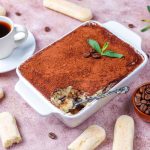 Una teglia di Tiramisù accanto a caffè e savoiardi