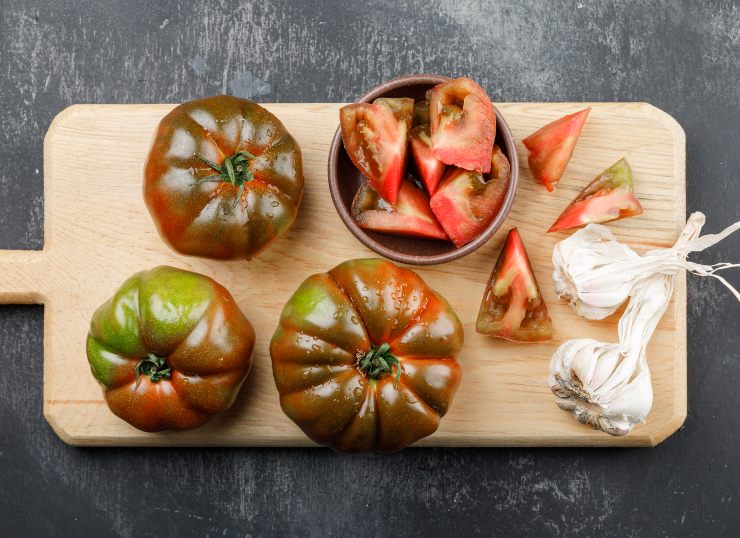 Pomodori cuore di bue interi e a fette su un tagliere vicino all'aglio